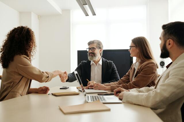 four people in a meeting, two of them are shaking hands